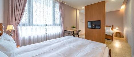 Quarto de hotel com uma cama grande, uma escrivaninha, uma cadeira, uma televisão na parede e uma mesinha de cabeceira.