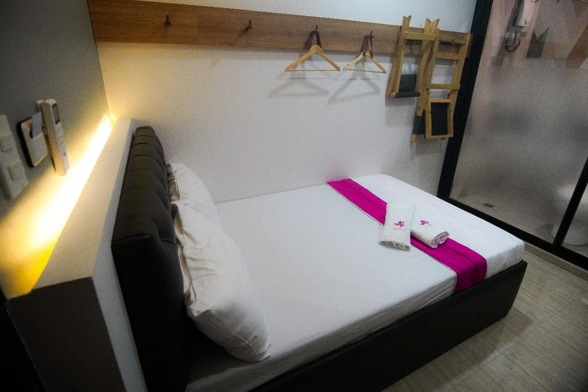 A hotel room with a bed, a wooden headboard, a wall-mounted towel rack, and a bedside table.