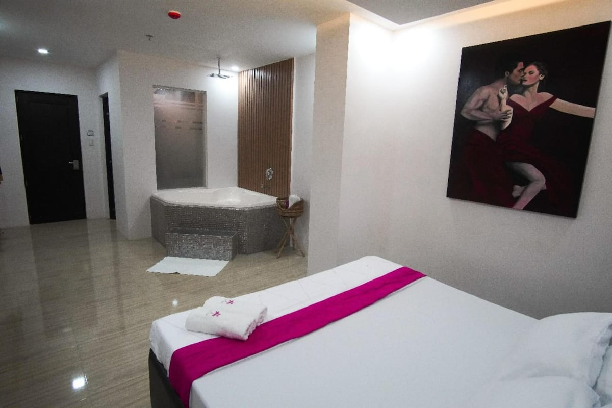 A hotel room with a large bed, a bathtub, and a painting on the wall.