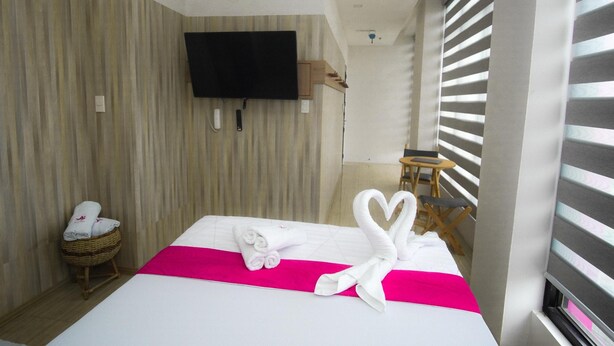 A hotel room with a bed, a television mounted on the wall, a small table, and a window with blinds. - OYO 1030 AI Hotel (Caloocan)