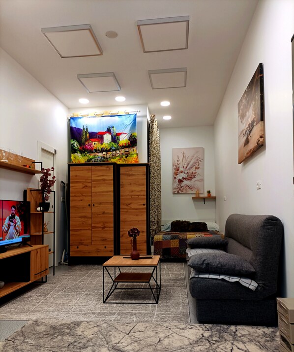 A living room with a TV, wooden furniture, a sofa, a patterned rug, and artwork on the walls.