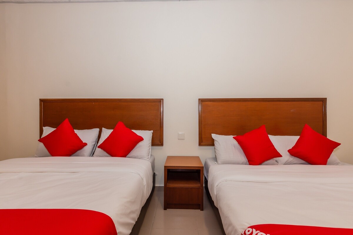 A hotel room with two beds, each with a wooden headboard and white bedding. There is a small wooden nightstand between the beds.