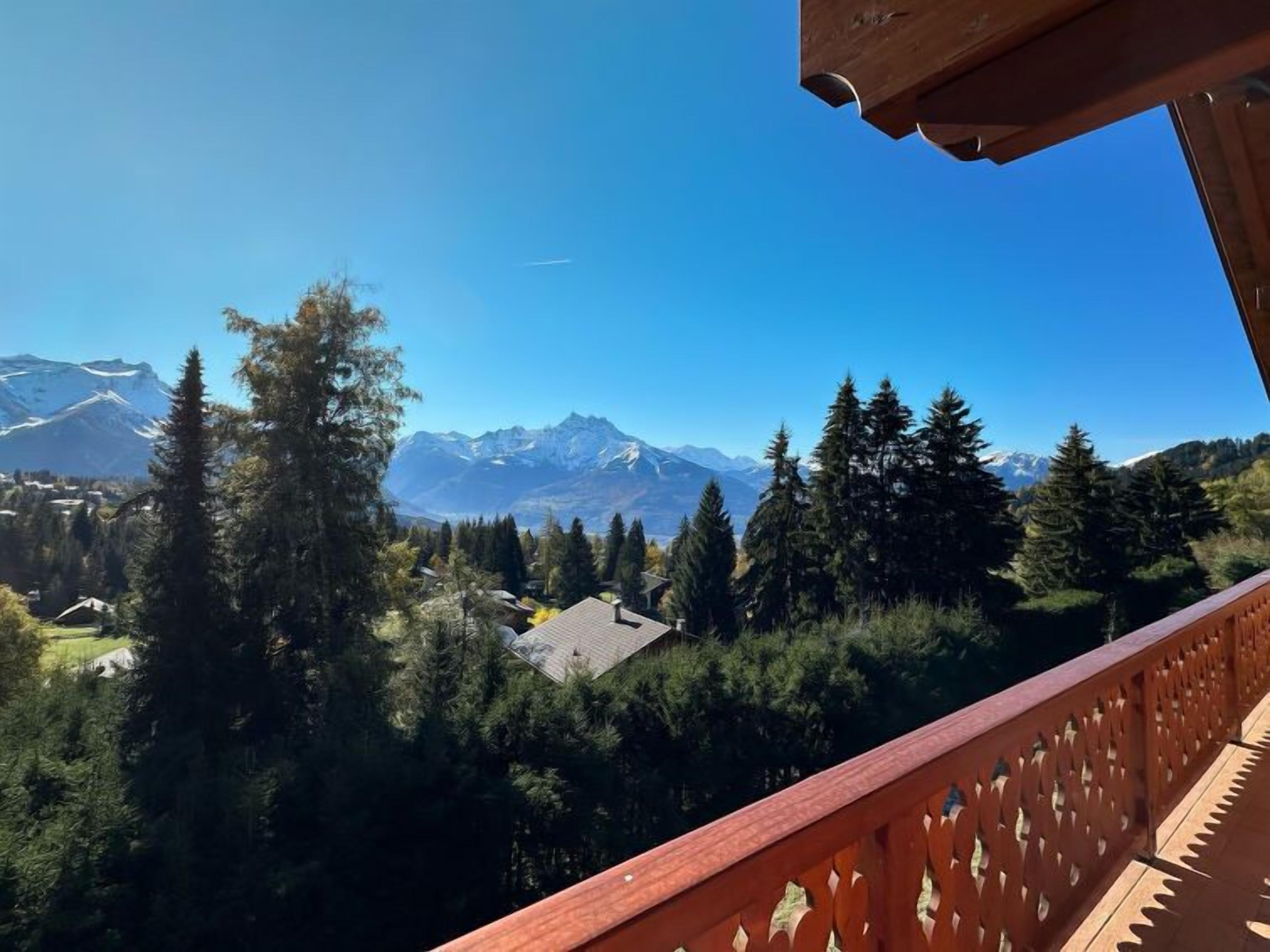 Un balcon offrant une vue sur des montagnes enneigées, une forêt dense et un petit bâtiment situé au loin.