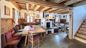 A rustic interior with exposed wooden beams, a wooden dining table with benches, a sofa, and a fireplace.