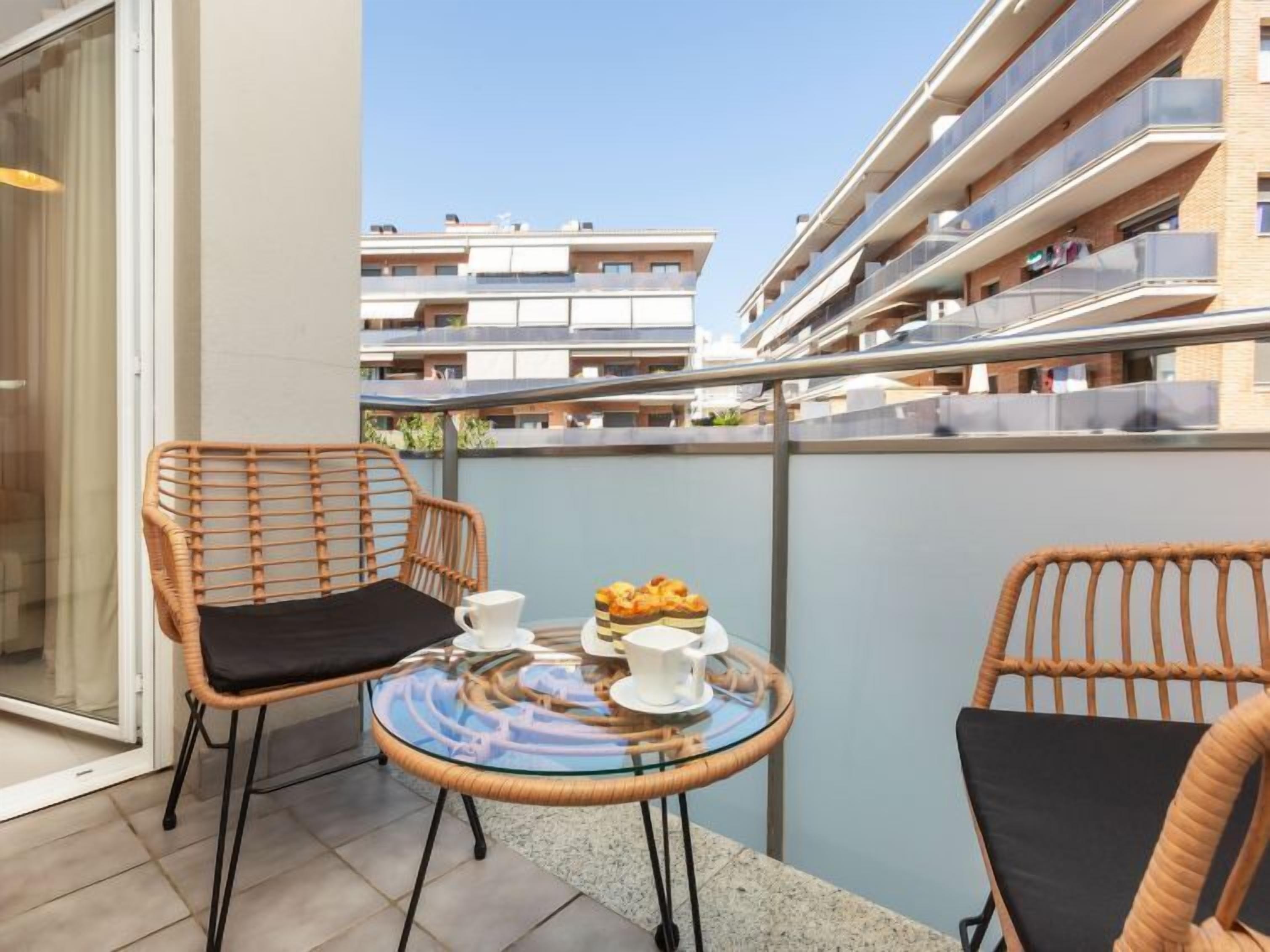 Un balcon avec des fauteuils en osier, une table en verre et un petit coin aménagé pour le petit-déjeuner.