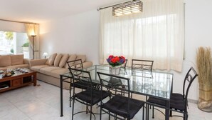 A modern living room with a glass dining table, black chairs, a beige sofa, and a large window with sheer curtains. - Nautic Par by Interhome (Playa de Aro)
