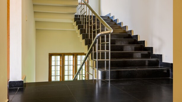 Una escalera con escalones negros y barandilla de metal, que lleva a un rellano con una puerta de madera y una ventana.