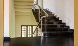 A staircase with black steps and a metal handrail, leading to a landing with a wooden door and a window. - Itsy Hotels Classiyo Munnar Crown Resorts (Devikolam)