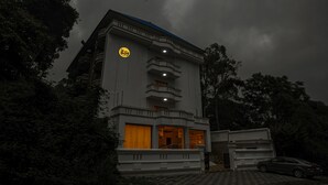 Un edificio de varios pisos con un logotipo destacado en la fachada, un balcón y un coche estacionado frente a él.