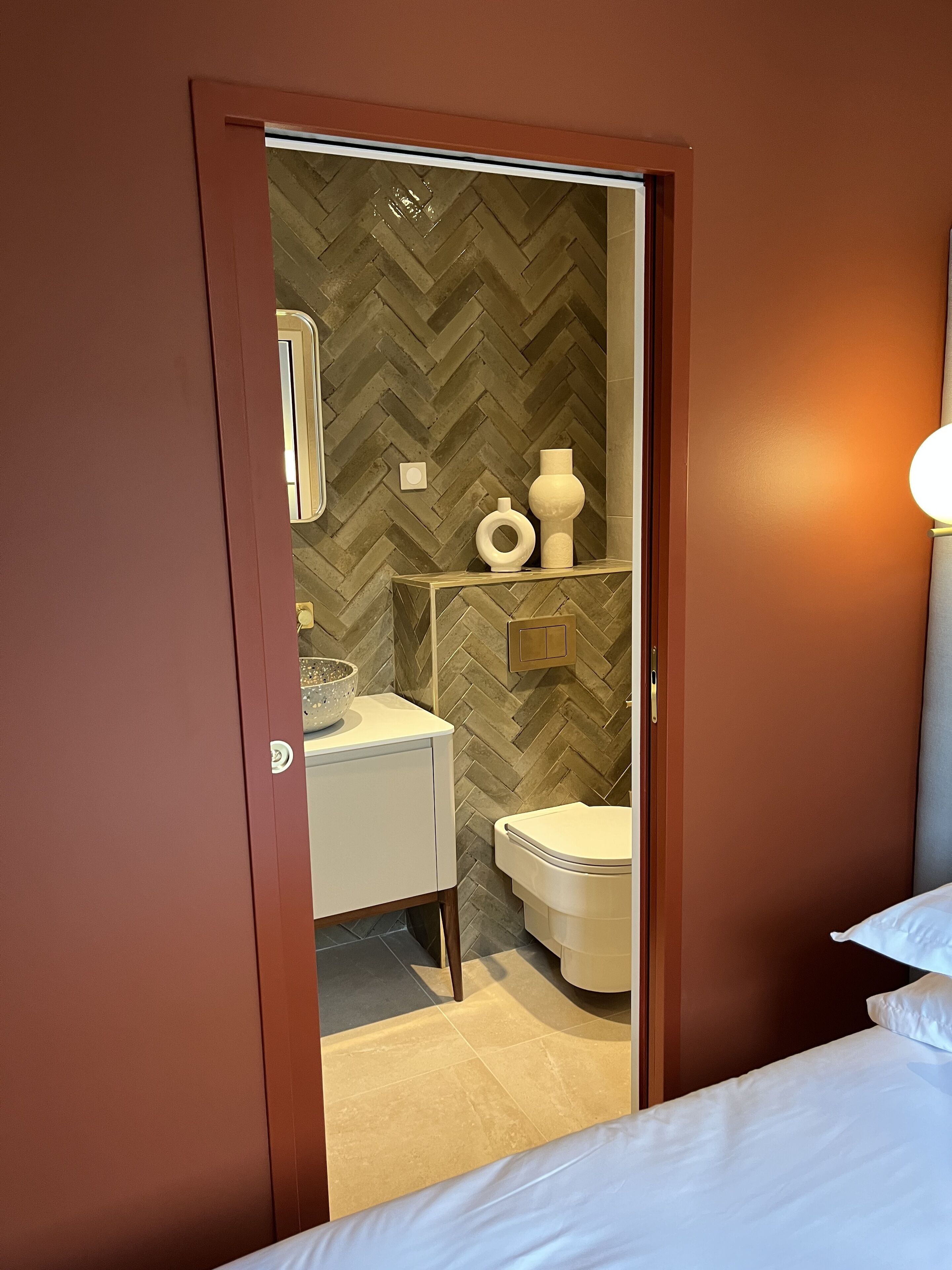 Et hotelværelse med en seng, et badeværelse med et chevronmønstret væg, en hvid vask og et toilet.