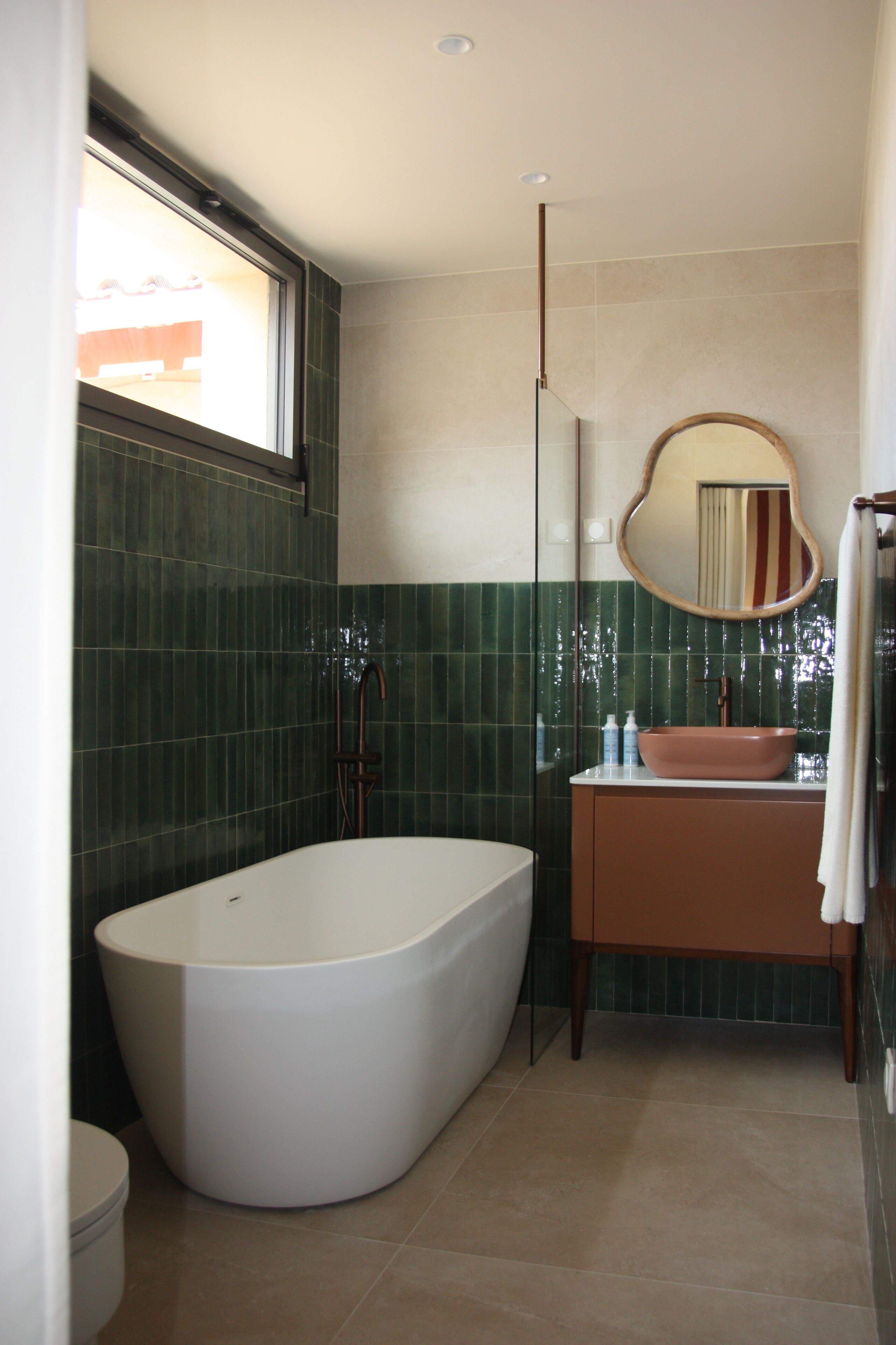 Un baño moderno con una bañera independiente, un tocador con espejo y paredes de azulejos verdes.