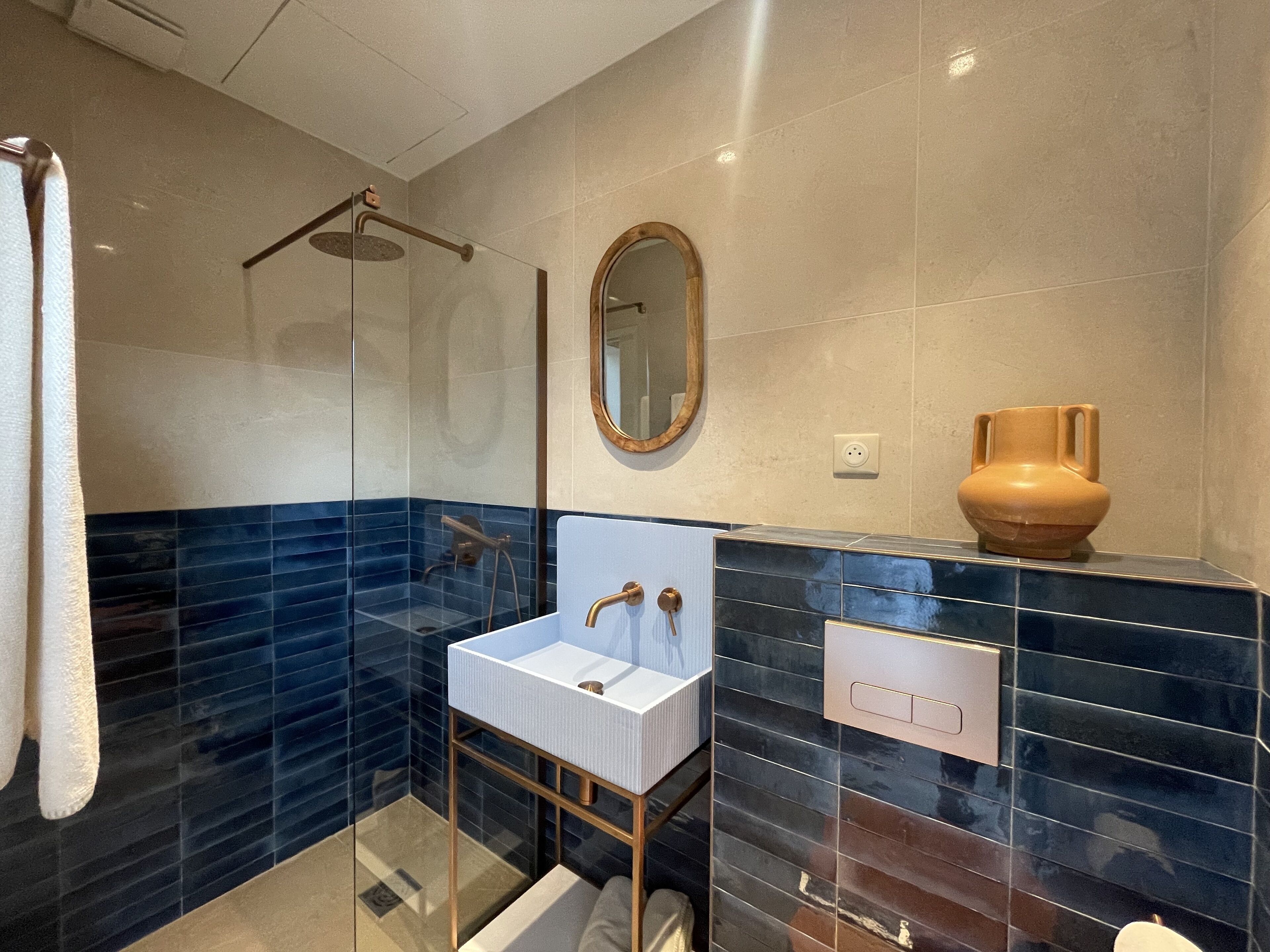 A modern bathroom with a glass-enclosed shower, a white sink with gold fixtures, and a decorative vase on the counter.