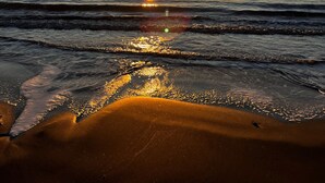Um pôr do sol sobre uma praia com ondas calmas e céu limpo.