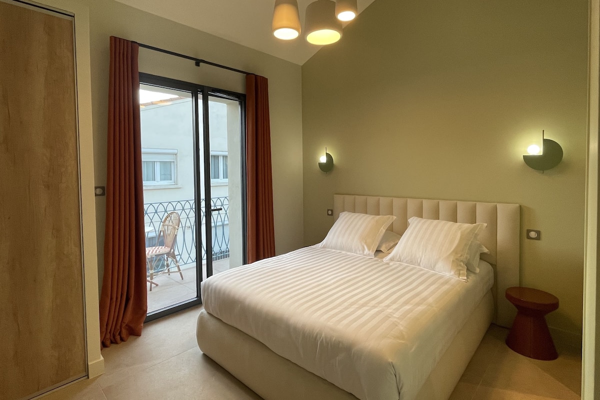 Un dormitorio con una cama grande, un ventanal corredero a un balcón y dos luces fijadas a la pared.