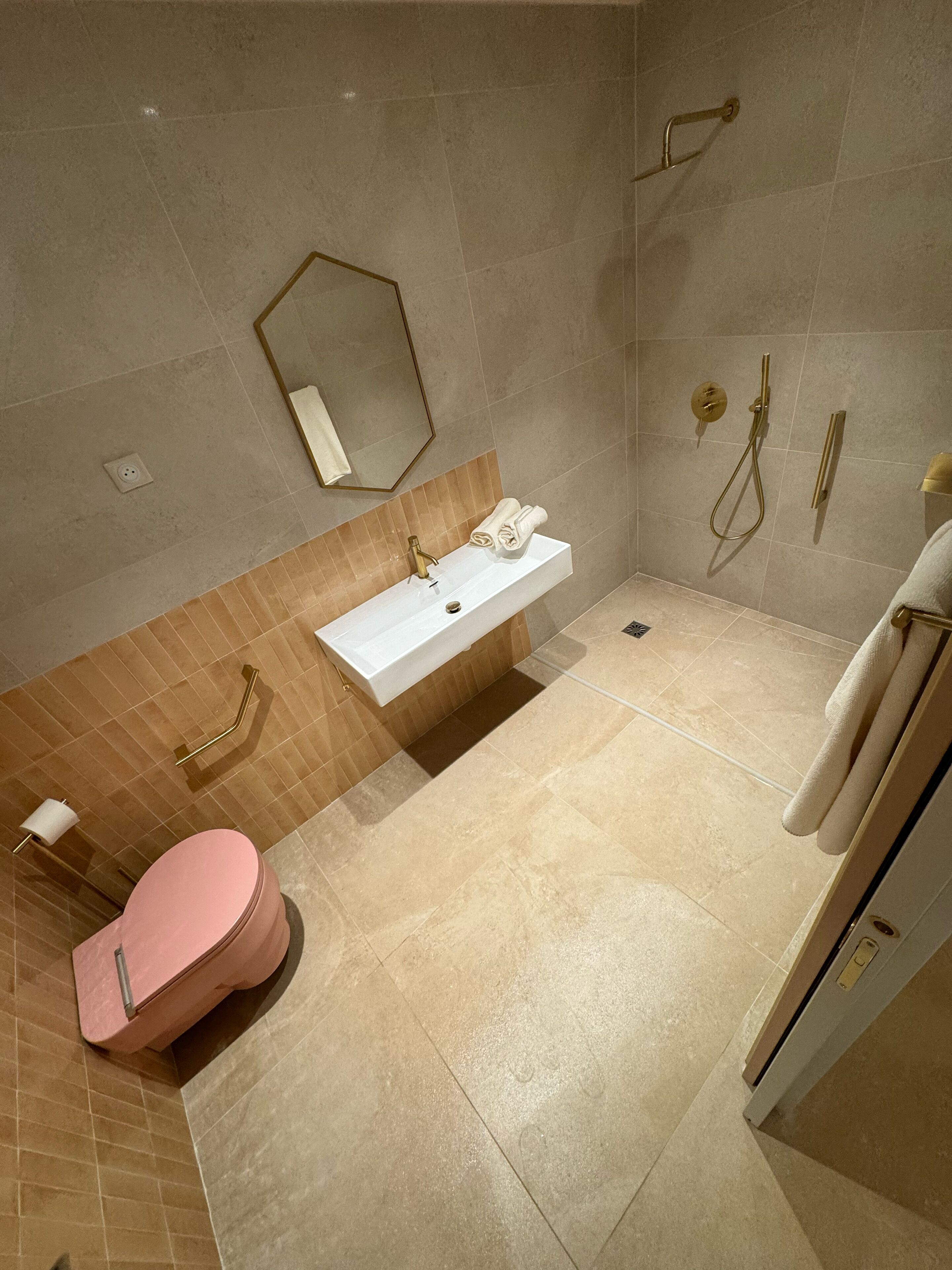 Ein Badezimmer mit weißem Waschbecken, einer rosa Toilette, einer Duschkabine und einem Handtuchhalter.