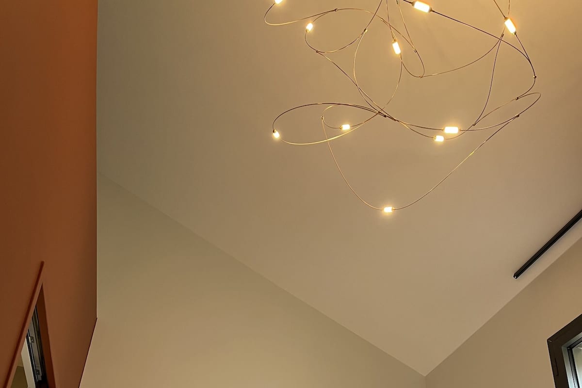 Un dormitorio con techo inclinado, una cama con almohadas blancas y dos lámparas fijadas a la pared.