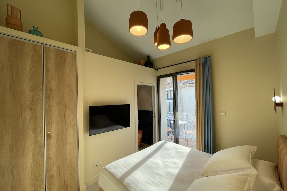 Un dormitorio con cama, armario, televisión montada en la pared y balcón con vistas.
