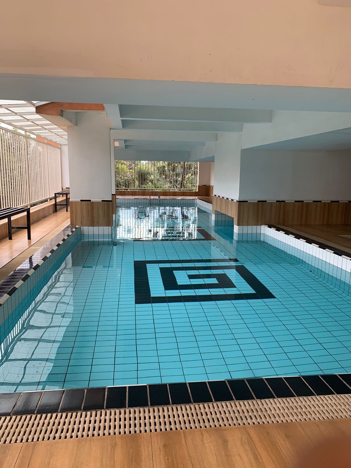 Une piscine intérieure dotée d’un carrelage aux motifs géométriques, d’un plancher en bois et offrant une vue sur les arbres à travers de grandes fenêtres.