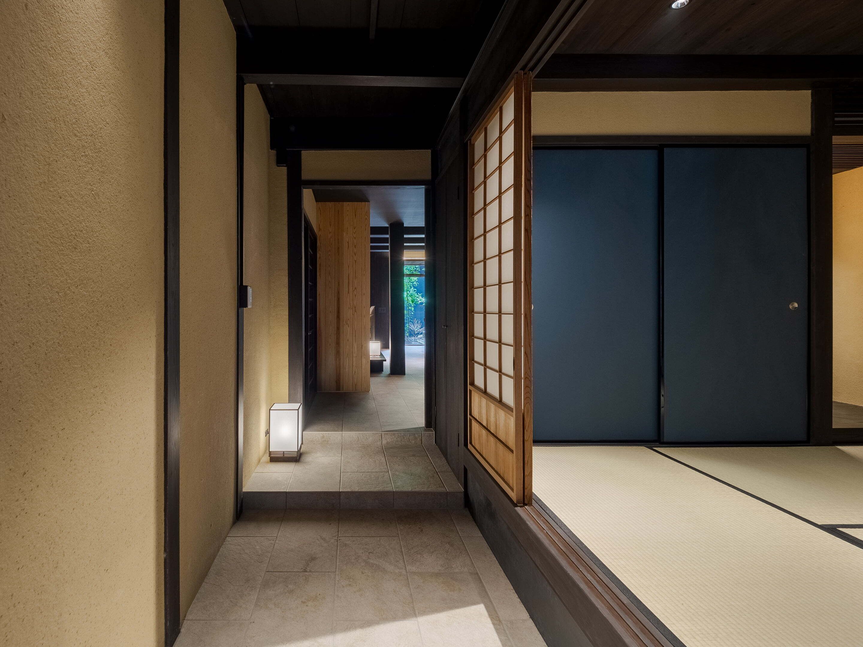 Un intérieur japonais traditionnel avec un sol recouvert de tatamis, des portes coulissantes et un couloir menant à une pièce.
