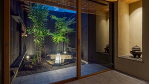Un intérieur de style japonais traditionnel, avec des portes coulissantes, une lanterne en pierre et un petit jardin agrémenté de plantes et d’un élément décoratif aquatique.