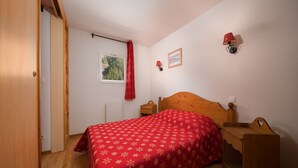 Ein Schlafzimmer mit einem hölzernen Bett, einem Nachttisch, einem Fenster mit Blick auf einen Wald und einem roten Vorhang.