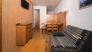 Ein gemütliches Zimmer mit einem hölzernen Schminktisch, einem Bett mit gestreifter Bettwäsche, einem Esstisch mit Stühlen und einer Deckenleuchte.