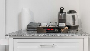 A kitchen counter with a coffee maker, a kettle, a toaster, and a stack of towels. - Meleys' Crimson Keep: Driftmark's Suite (Seattle)