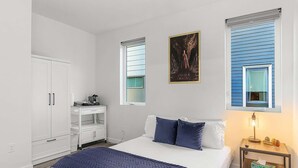 A bedroom with a bed, a desk, a wardrobe, and two windows with blinds. - Meleys' Crimson Keep: Driftmark's Suite (Seattle)