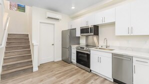 A modern kitchen with white cabinets, stainless steel appliances, and a wooden staircase. - Meleys' Crimson Keep: Driftmark's Suite (Seattle)