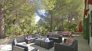 An outdoor seating area with wicker furniture and a table, surrounded by trees. - Teresa - beautiful house 150 meters from the beach (Alcúdia)