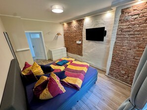 Een slaapkamer met een bed, een witte dressoir, een bakstenen muur en een wandtelevisie.