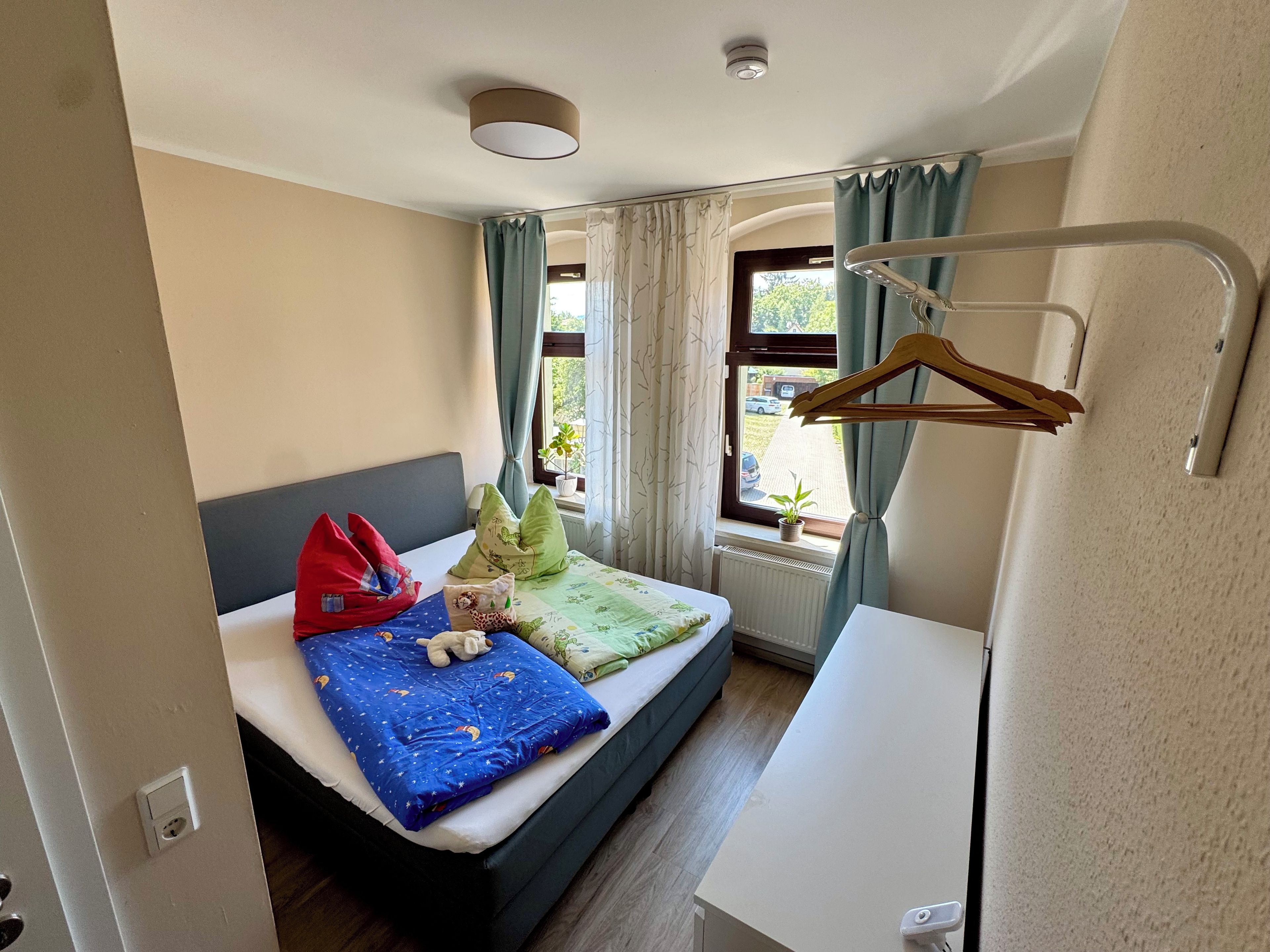 A compact hotel room with a bed, bedside table, and a window with curtains.