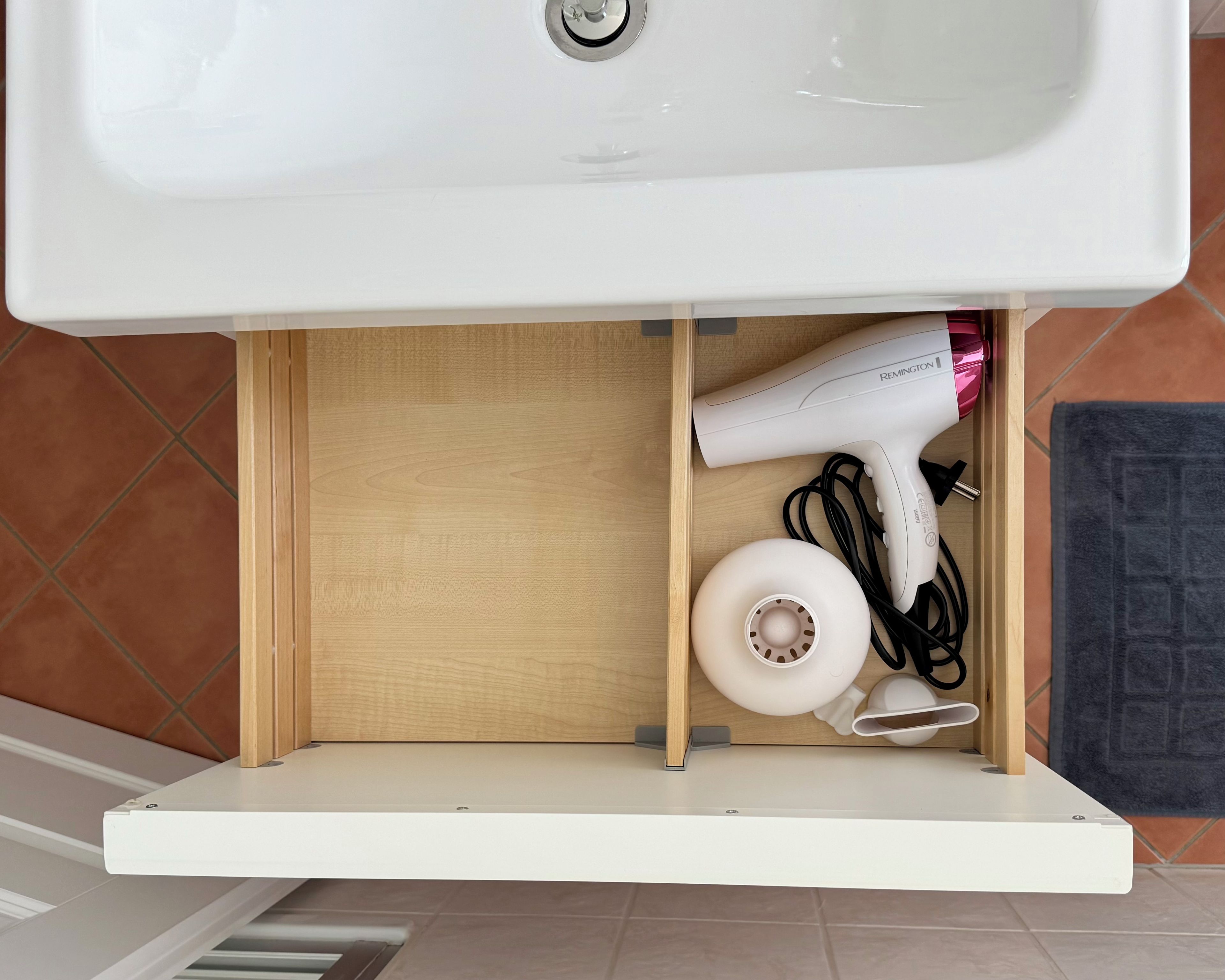 A bathroom with a white sink, a wooden vanity, and a hairdryer stored under the sink.