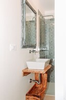 Un baño con lavamanos blanco, tocador de madera y un espejo.