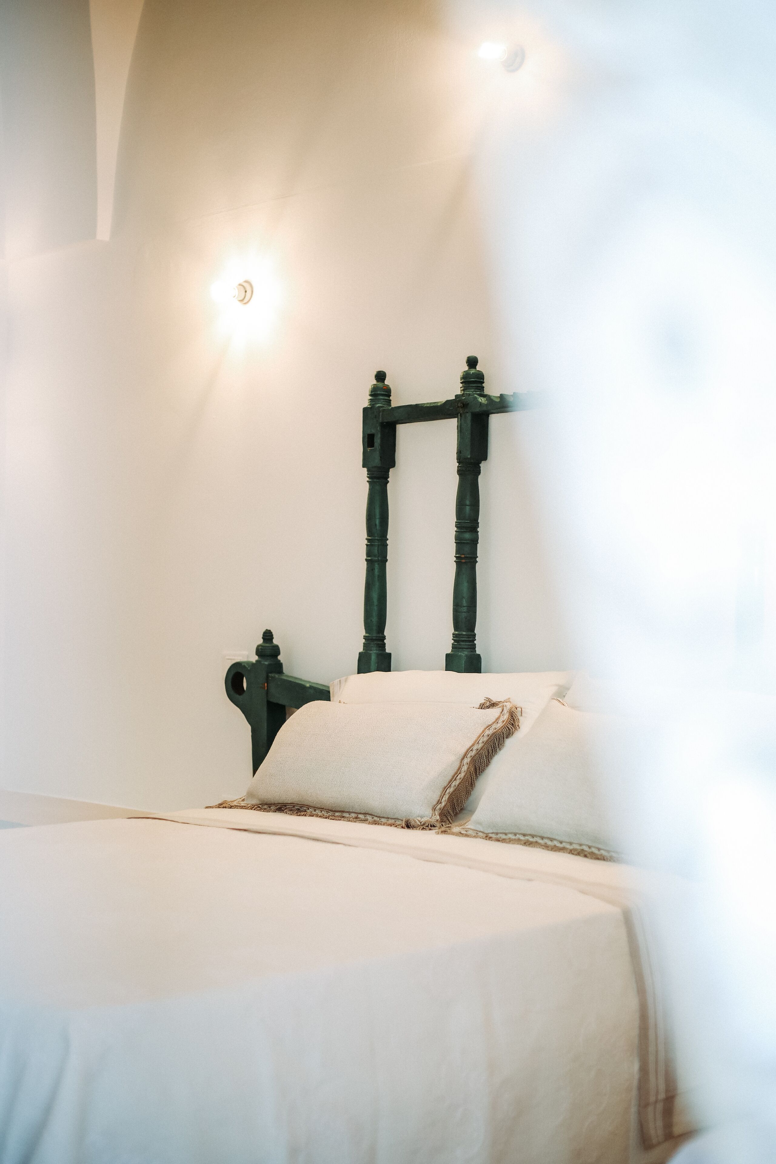 A bed with a white mattress and pillows, a wooden headboard, and a wall-mounted light fixture.