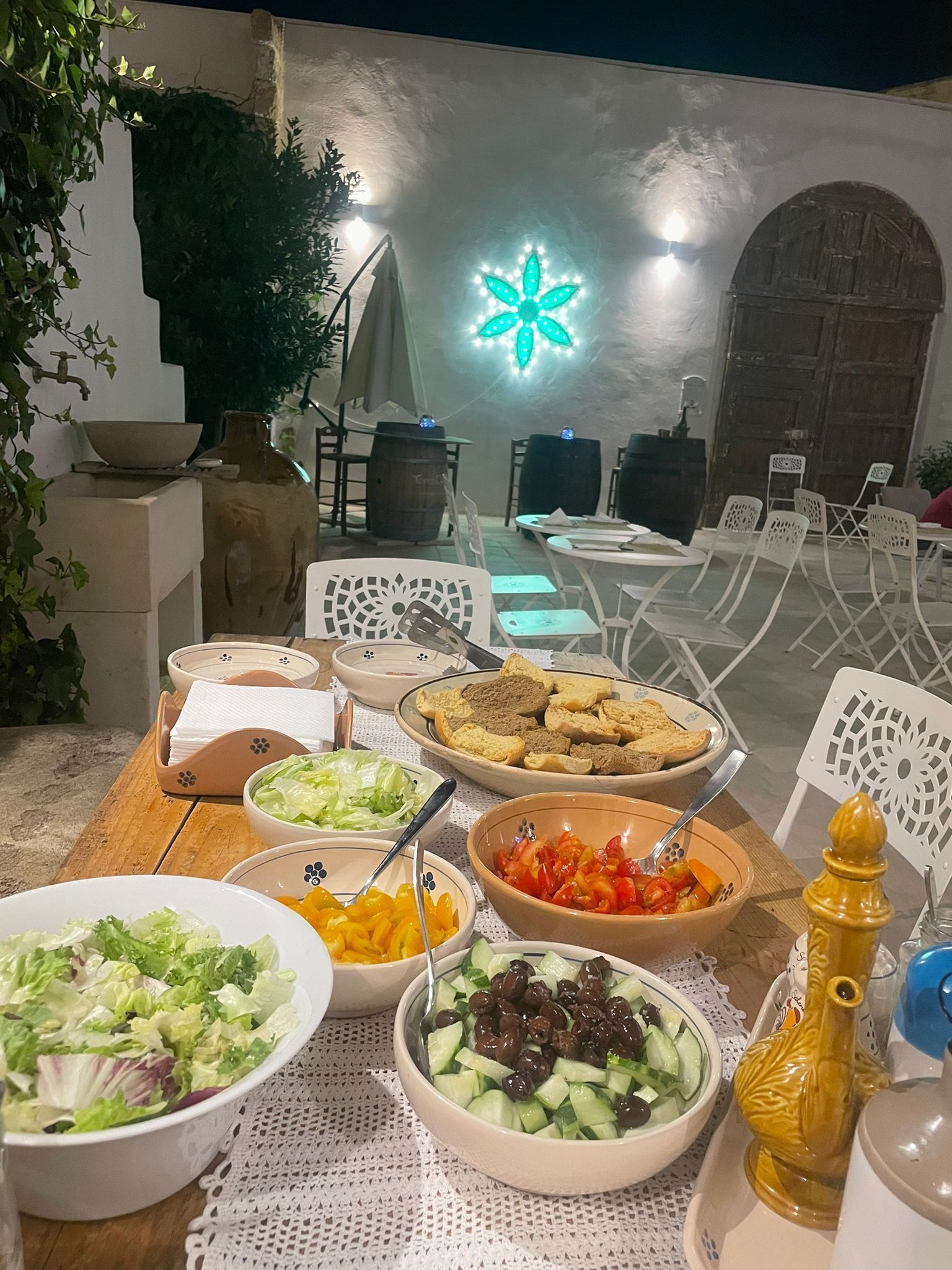 Ein Essbereich im Freien mit Tisch, gedeckt für eine Mahlzeit, umgeben von weißen Stühlen und einer dekorativen Leuchte im Hintergrund.