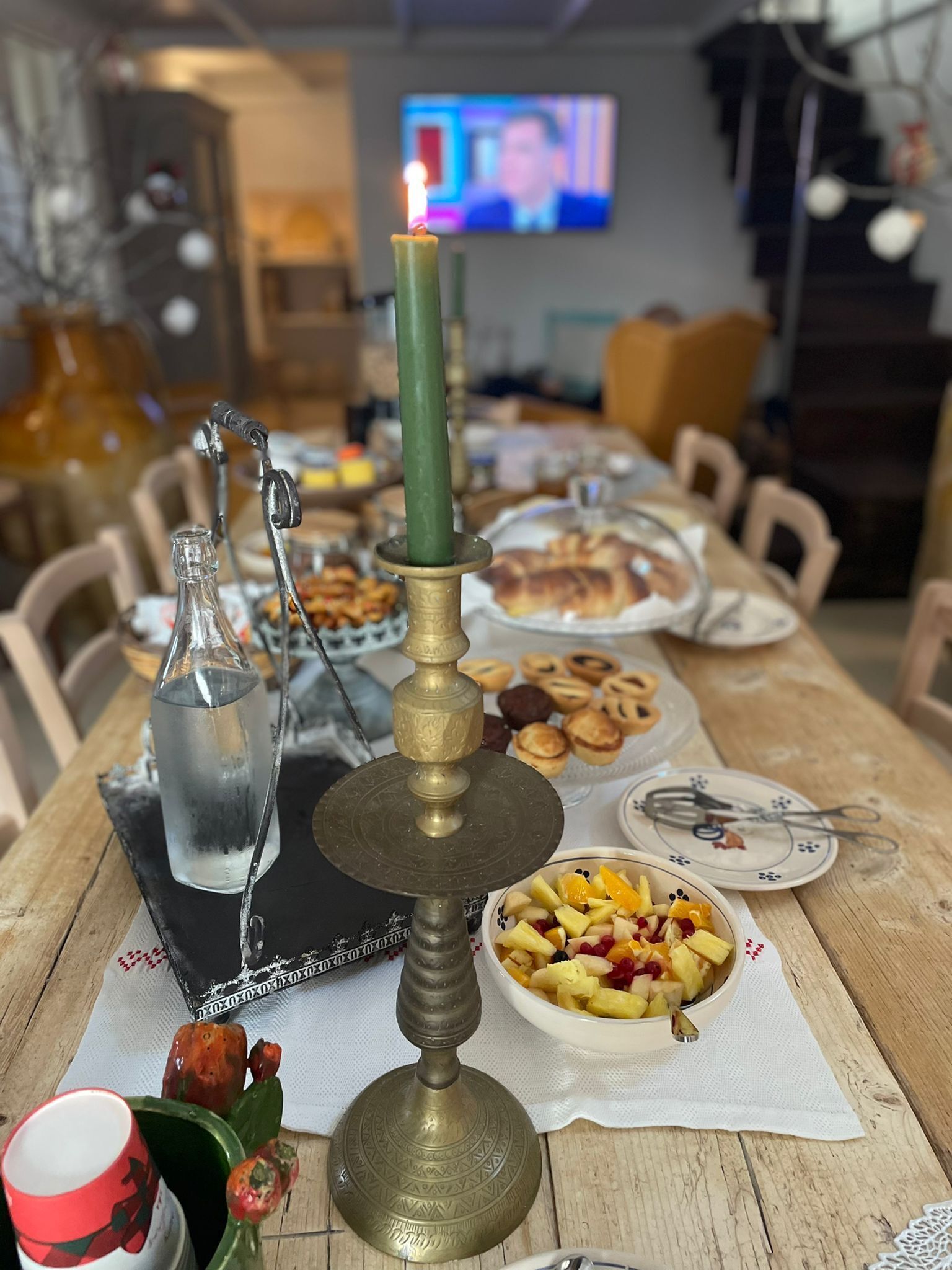 A dining table with a candle, a bottle, and a bowl of fruit.