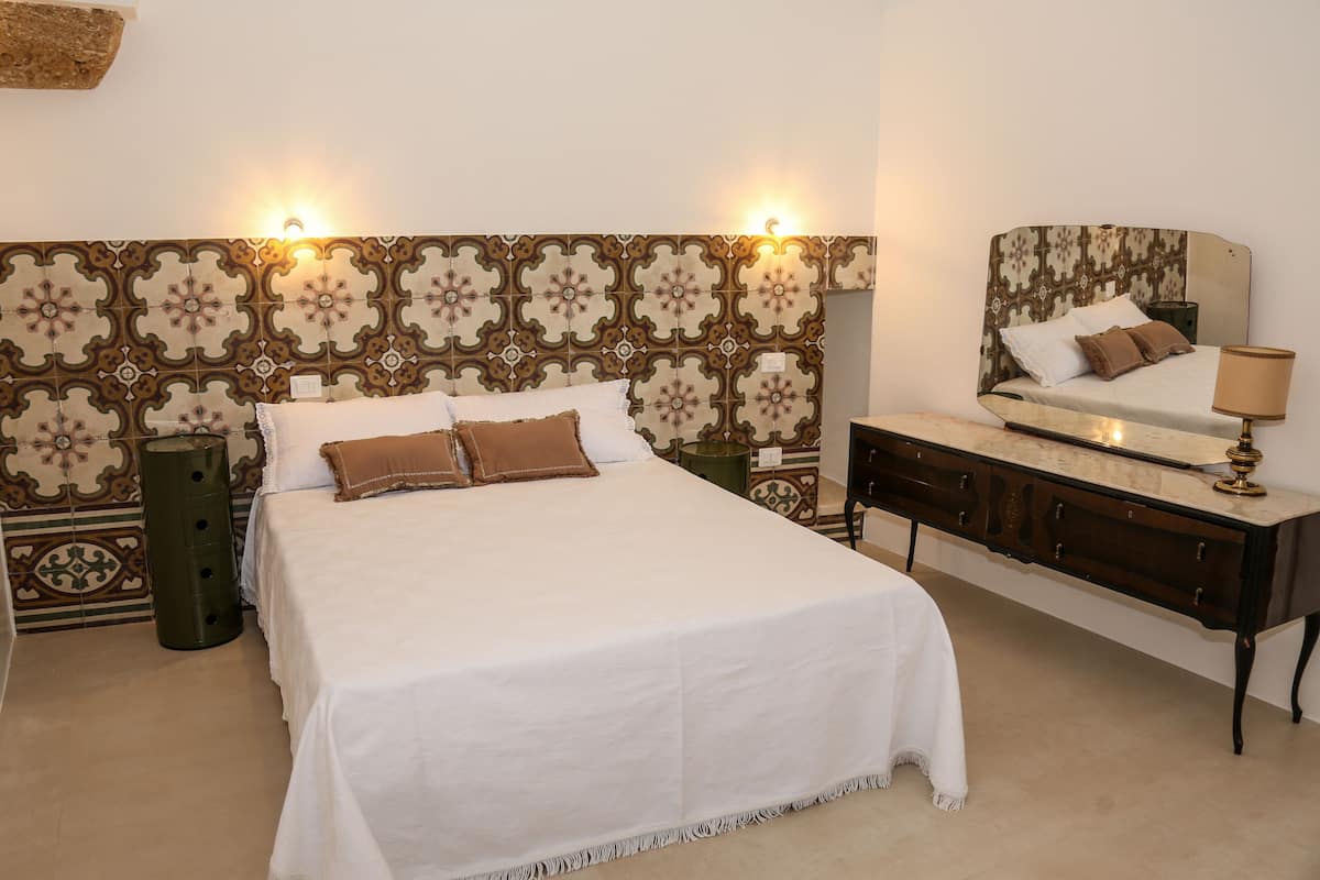 A neatly arranged bedroom with a large bed, a dresser, and a mirror.