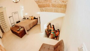 A bedroom with a bed, a wooden side table, a chair, a small table with a lamp, and a wall-mounted light fixture. - Corte Largo Lauro Dimore&Spa (Ugento)