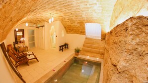 A spa area with a stone-walled pool, wooden seating, and a mirror with lights. - Corte Largo Lauro Dimore&Spa (Ugento)