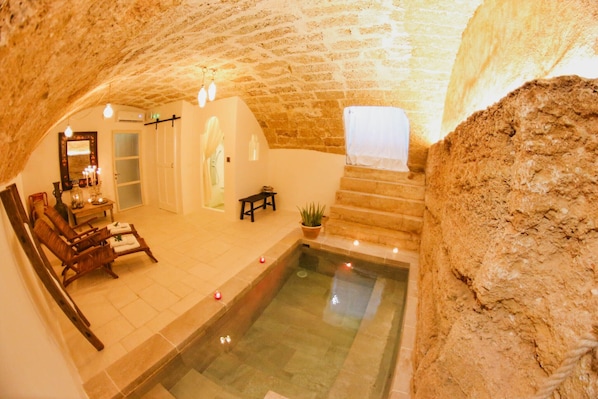 Un área de spa con piscina de paredes de piedra, asientos de madera y un espejo con luces.