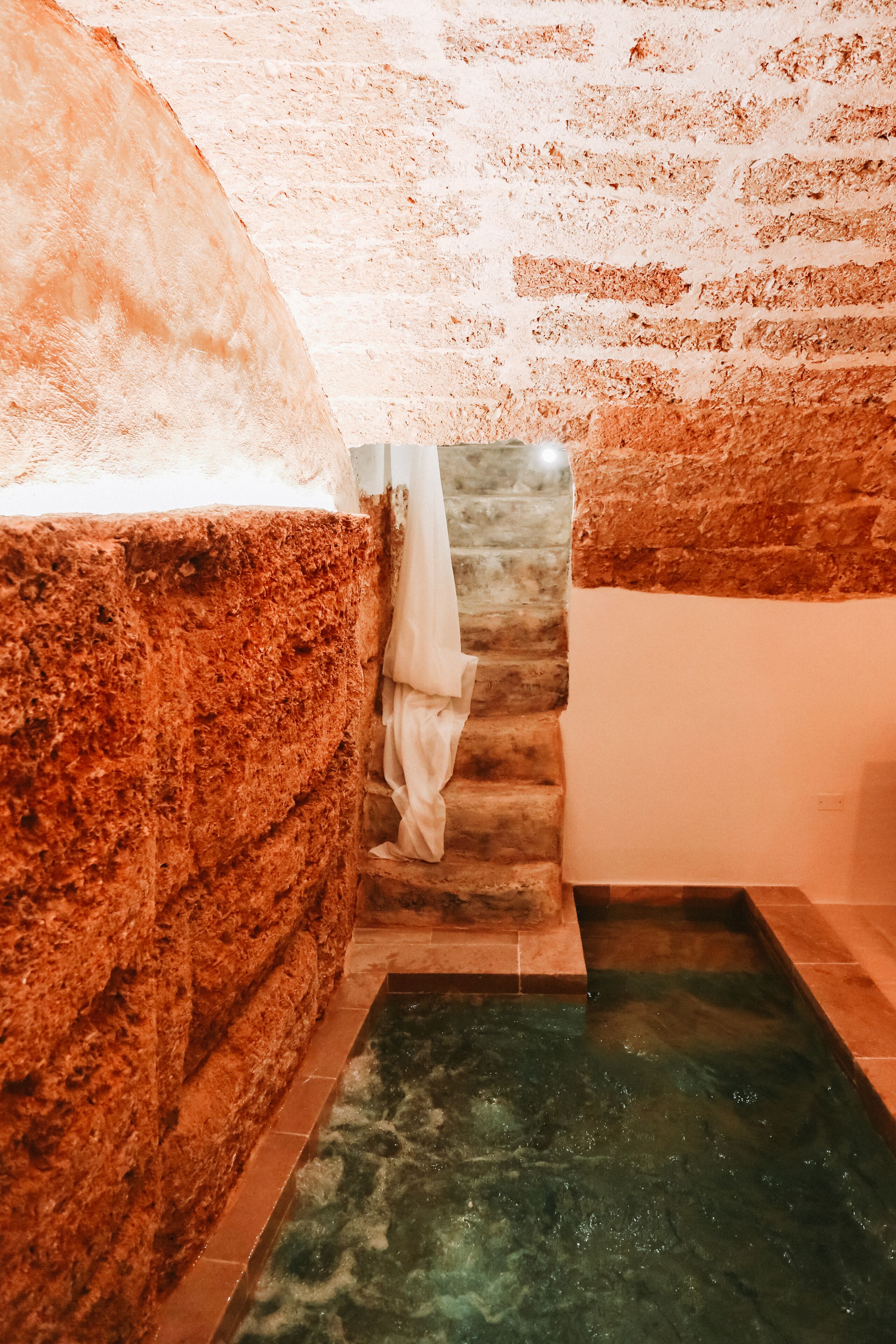A bathroom with a stone wall, a tiled floor, and a small pool.