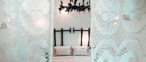 A bedroom with a bed, a chandelier, and lace curtains.