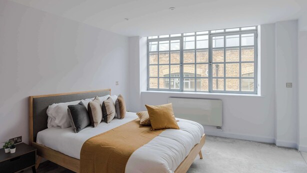 Een slaapkamer met een bed, een raam, een radiator en een nachtkastje.