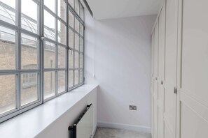 A narrow hallway with a radiator, a window with a view of a brick building, and a set of white doors. - Clerkenwell 3-Bed Apartment · Lift · Sleeps 8 (Greater London)