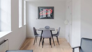 A modern dining area with a table and chairs, a framed picture on the wall, and a window providing natural light. - Farringdon 1-Bed Apartment · Lift · Sleeps 3 (London)