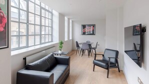 Une pièce moderne avec un canapé en cuir noir, une table à manger avec des chaises et une grande fenêtre donnant sur des immeubles.