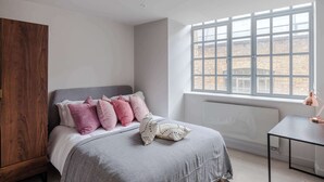 A bedroom with a bed, a wooden wardrobe, a radiator, and a window with a view of brick buildings. - Farringdon 1-Bed Apartment · Lift · Sleeps 3 (London)
