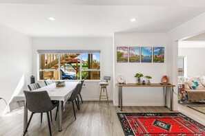 A modern dining area with a large table, chairs, and a view of the outside. There is a console table with decorative items and a rug on the floor. - Spacious Renovated 3BR in Ellerslie I Zodiak Stays (Auckland)