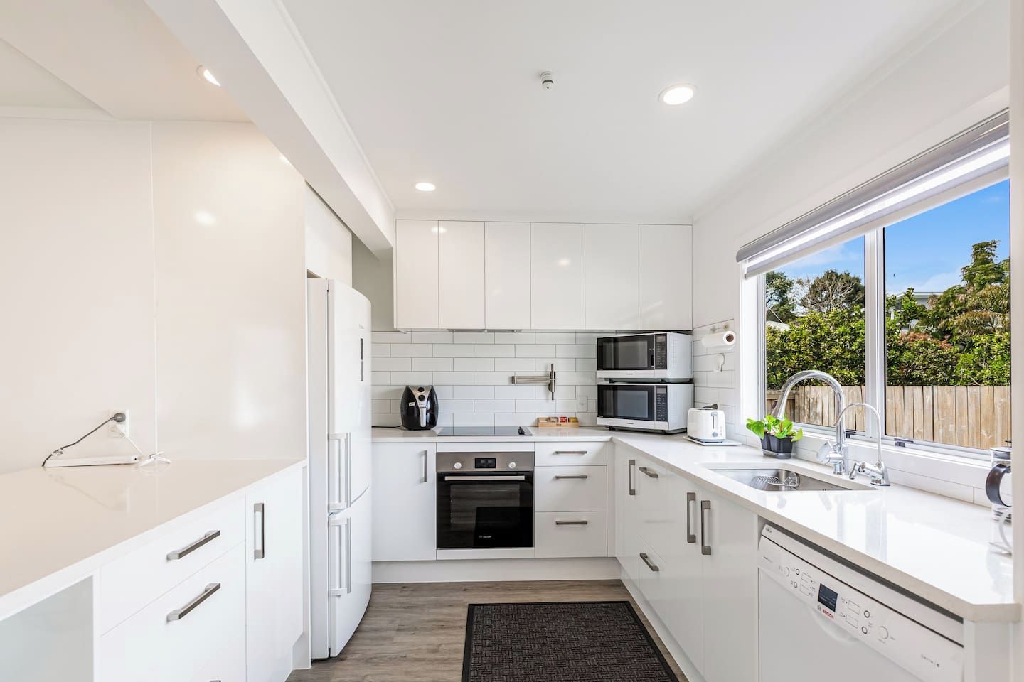 A modern kitchen with white cabinetry, a built-in oven, a microwave, and a sink with a window view.